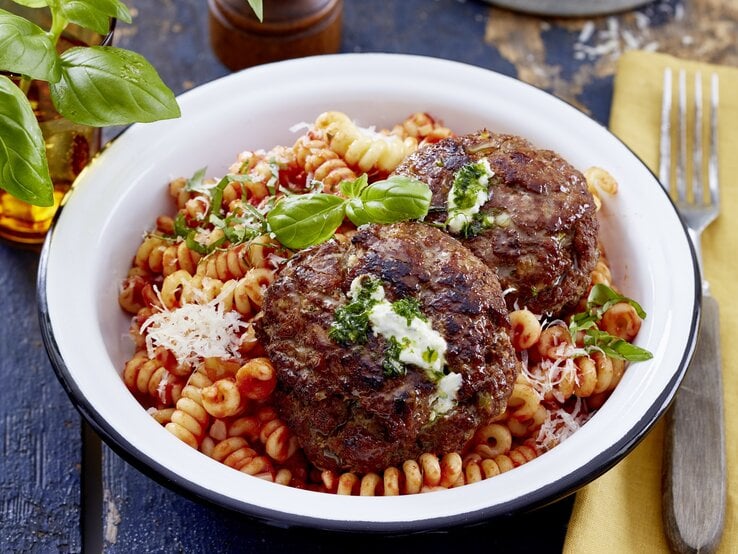 In einer Schüssel ist eine Portion Frikadellen mit Pesto-Ricotta-Füllung und Nudeln. Das Gericht ist verfeinert mit Parmesan und Basilikum. 