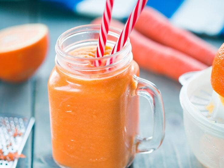 Ein Glas mit dem Karotten-Orangen-Smoothie auf einem dunkelblauen Tisch.