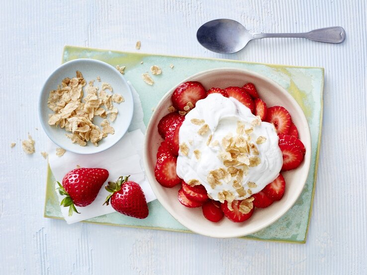 Nichts geht über ein süßes Frühstück! Mit unseren Erdbeeren mit Vanillequark zauberst du in nur 10 Minuten etwas Leckeres auf den Tisch! In einer Schüssel sind Erdbeeren mit Vanillequark angerichtet. Darüber sind Dinkel-Flocken gegeben.