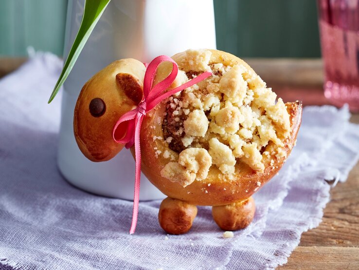 Eins der Streusel-Lämmer aufrecht und mit Schleife vor einer Blumenvase.