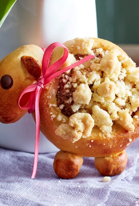Eins der Streusel-Lämmer aufrecht und mit Schleife vor einer Blumenvase.