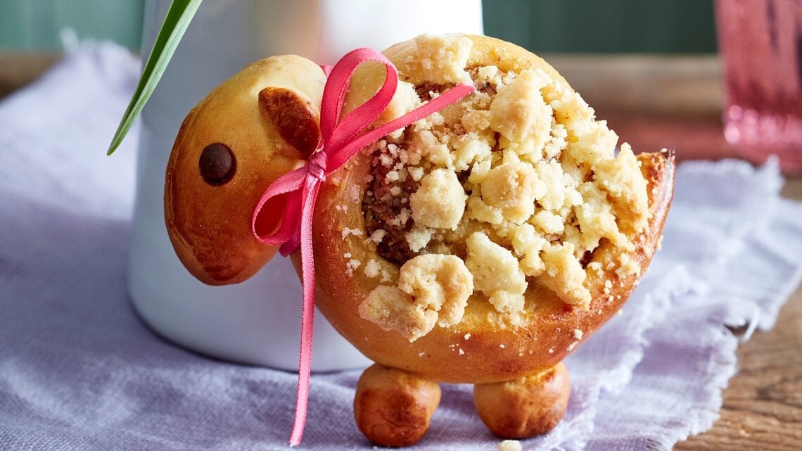 Eins der Streusel-Lämmer aufrecht und mit Schleife vor einer Blumenvase.