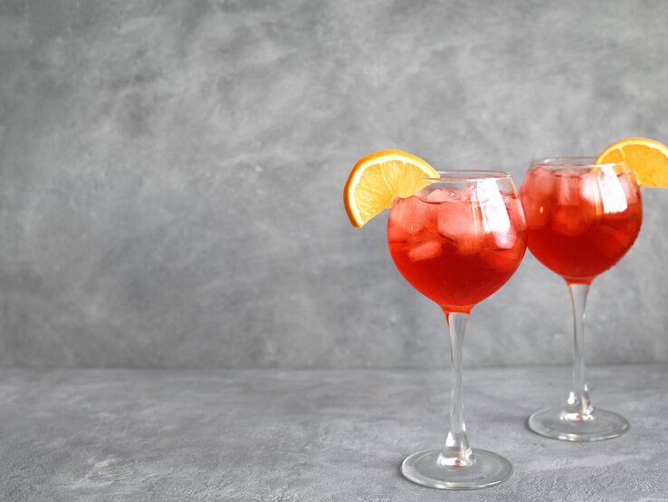 Zwei Gläser mit Negroni Spritz vor einem grauen Hintergrund.