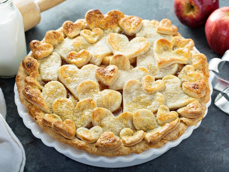 Auf einem Teller ist ein Apfel-Gitterkuchen mit Herzen serviert. Er hat Teigförmige Herzen oben drauf.