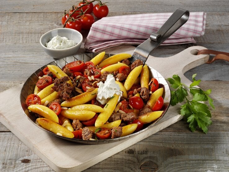 Gusseiserne Pfanne mit Schupfnudeln, Kirschtomaten und Hackfleisch auf einem Holztisch.