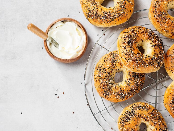 Mehrere Bagels auf einem Kuchengitter mit einer kleinen Schale Joghurt. Alles direkt von oben fotografiert.