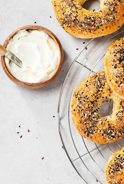 Mehrere Bagels auf einem Kuchengitter mit einer kleinen Schale Joghurt. Alles direkt von oben fotografiert.