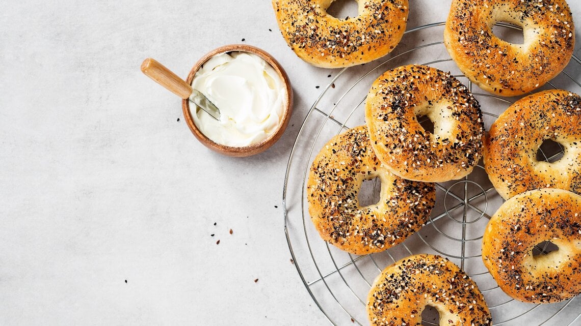 Mehrere Bagels auf einem Kuchengitter mit einer kleinen Schale Joghurt. Alles direkt von oben fotografiert.