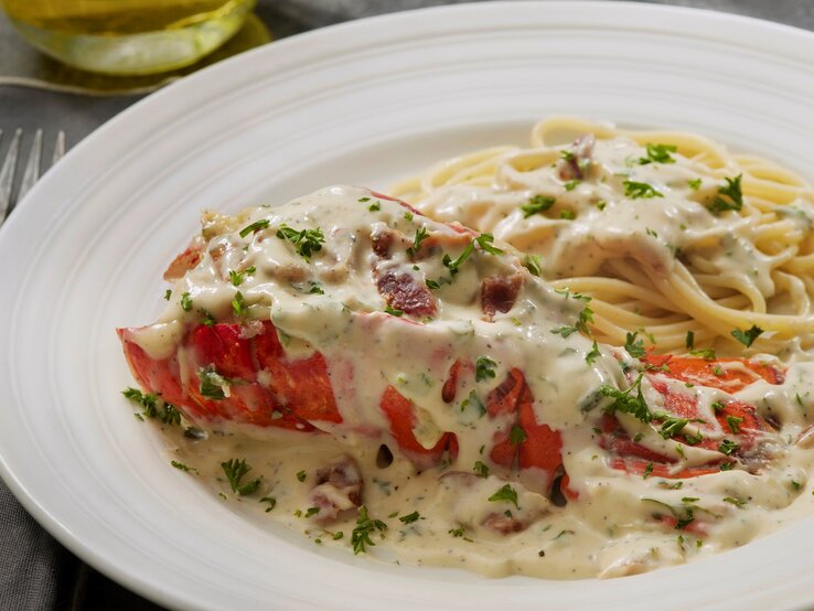 Ein weißer Teller mit Spaghetti der Carbonara-Soße und einem Hummer der mit Soße bedeckt ist.