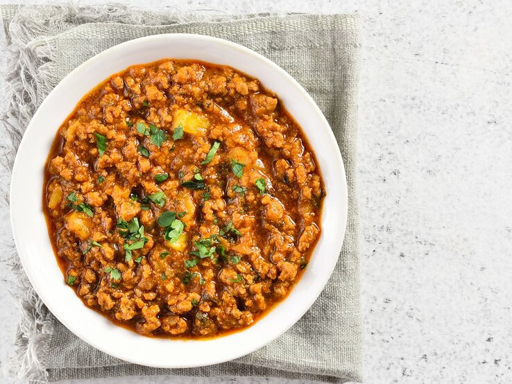 Eine weiße Schale mit dem rötlichen Curry auf einem hell-beigenen Leinentuch und einem weißen Tisch.