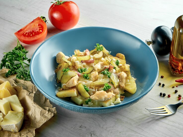 Was tun mit den Resten vom Raclette-Abend? Wir haben da eine Idee. Blauer Teller belegt mit einer Kartoffel-Käsepfanne mit Gurken.