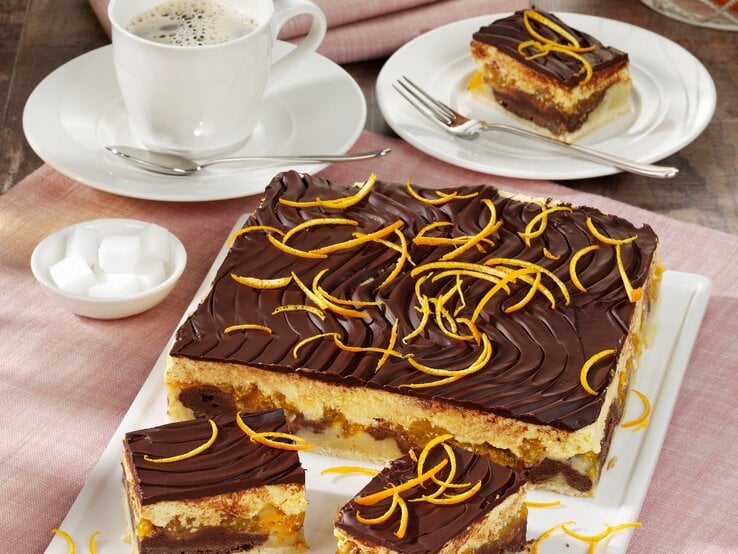 Auf einem Teller leigt eine Donauwelle mit Orangen und Mandarinen. Sie ist mit Schokoladenglasur überzogen und mit Orangenzesten bestreut. 