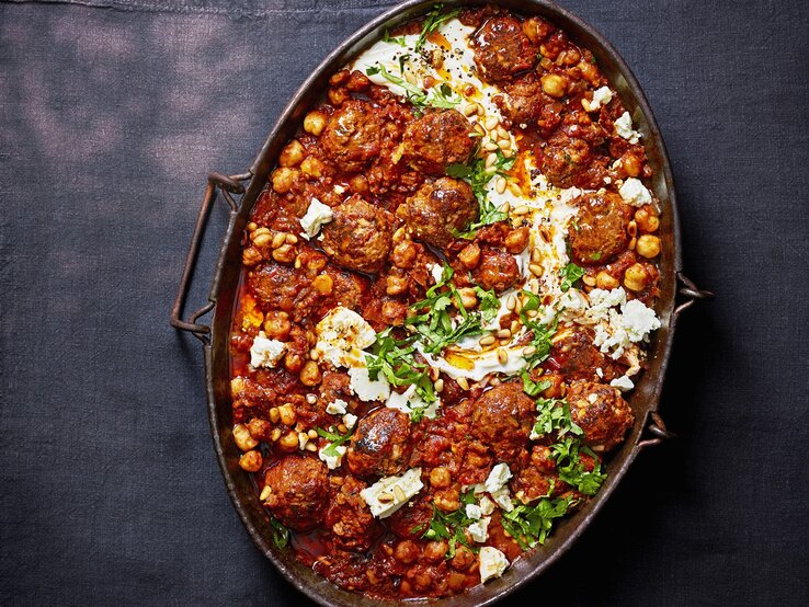 Harissa-Hackbaellchen-Feta Harissa-Hackbällchen mit Feta-Swirl in einer metallischen Auflaufform. Das Ganze auf einem dunklen Untergrund.