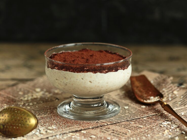 Ein Dessertglas mit Tiramisu-Porridge auf Zeitungspapier.