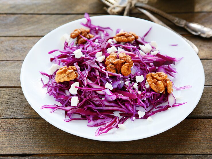Auf einem Tisch steht ein runter Teller mit Rotkohlsalat, Ziegenfrischkäse und Walnüssen / Draufsicht