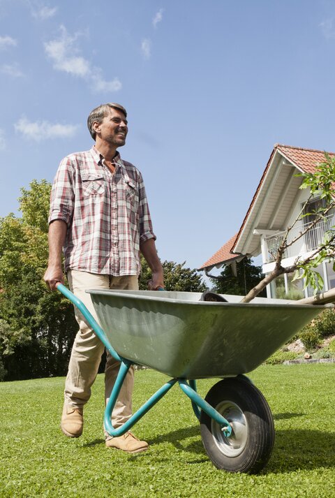 Ein Mann steht mit einer Schubkarre im Garten.