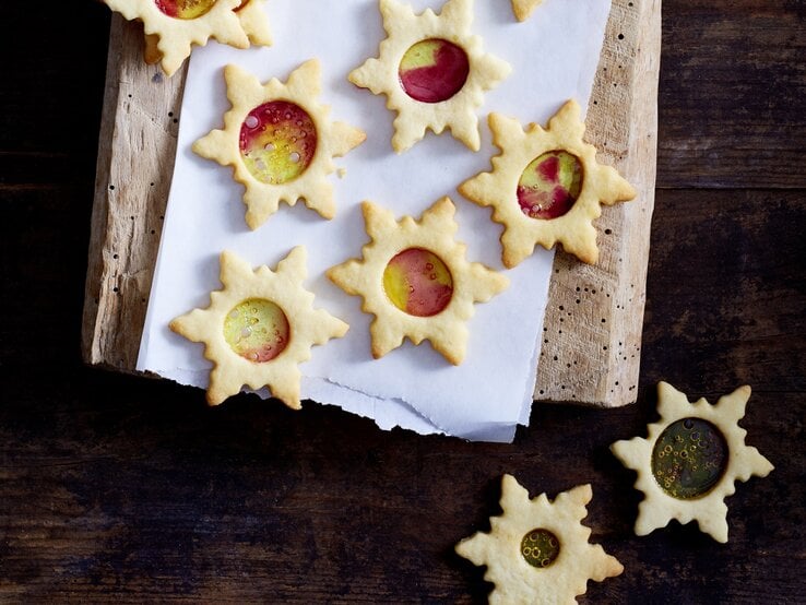 Mehrere Weihnachtssterne mit buntem Zucker liegen auf einem Holzbrett. 