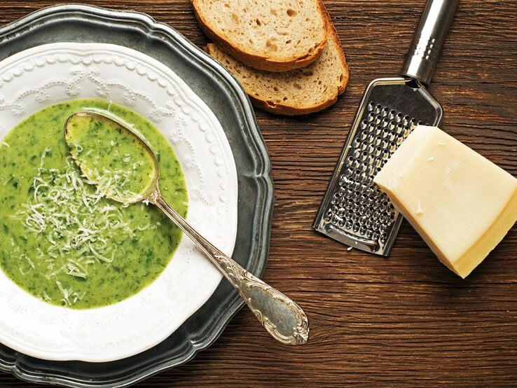 Mangoldsuppe mit frisch geriebenen Parmesan und zwei Scheiben Brot.