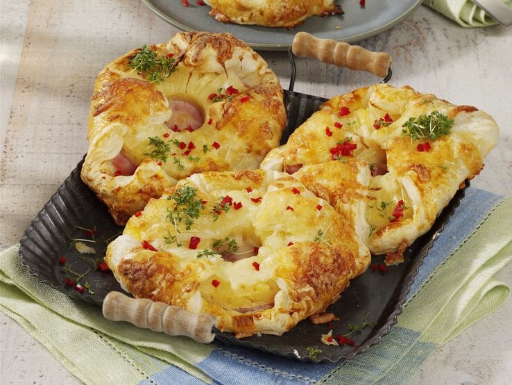 Kopenhagener Teilchen Hawaii Kopenhagener Teilchen Hawaii, mit Käse überbakcen und mit Petersilie und Chiliflocken garniert, serviert auf einem Tablett auf einem Küchentuch.