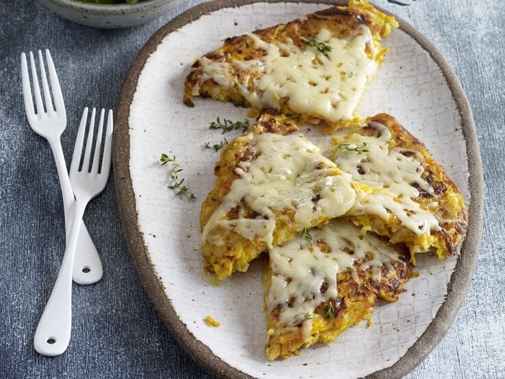 Auf einem Teller liegen Kürbis-Kartoffel-Rösti mit Bergkäse. Sie sind mit Käse überbacken. 
