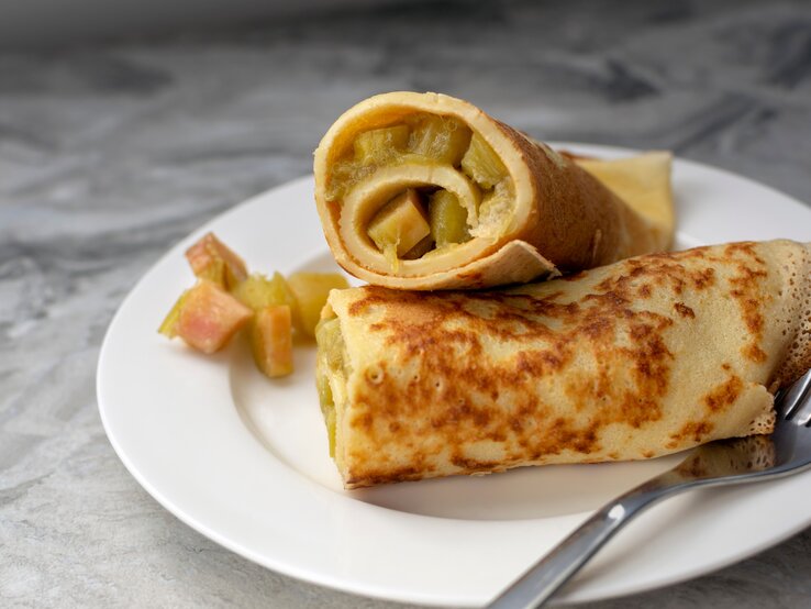Ein weißer Teller mit den gerollten Pfannkuchen und saftigem Rhabarber.