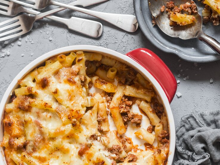 Eine rote Auflaufform mit den Ofen-Makkaroni alla mamma auf einem grauen Tisch. Alles direkt von oben fotografiert.