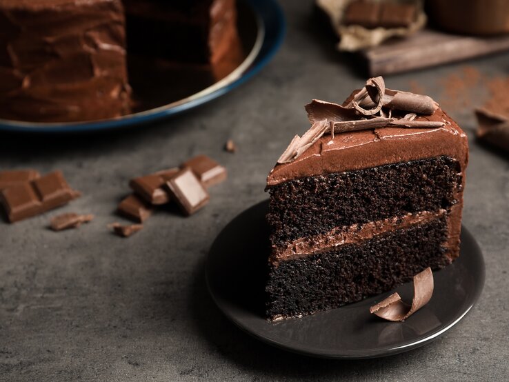 Ein Stück Schokotorte mit selbst gemachter Schokoladencreme auf einem Teller, im Hintergrund die angeschnittene Torte.