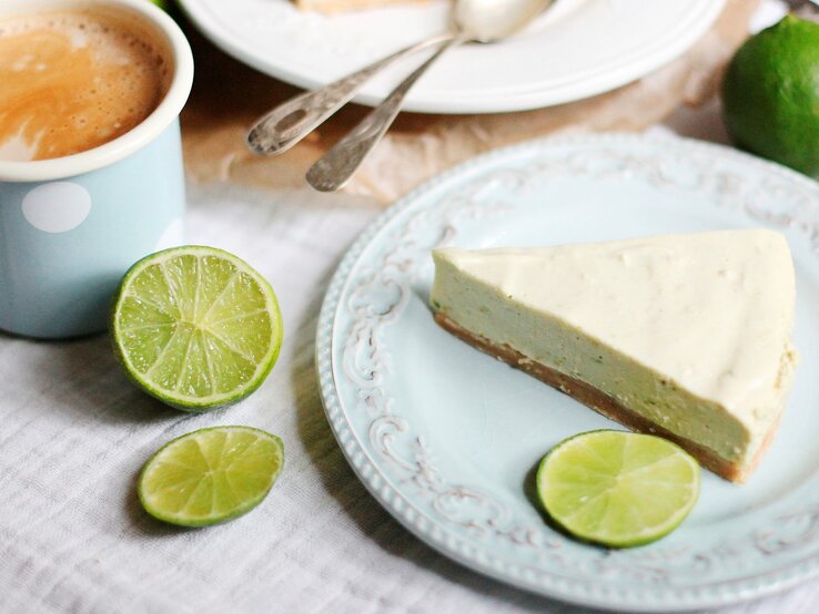 Ein Stück Mojito Torte auf einem Kaffeetisch mit hellblauer Tischdecke und Limetten