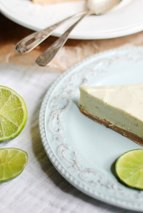 Ein Stück Mojito Torte auf einem Kaffeetisch mit hellblauer Tischdecke und Limetten