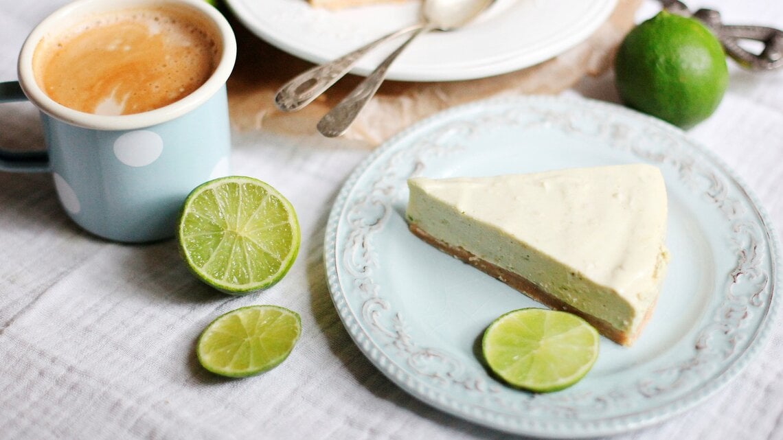 Ein Stück Mojito Torte auf einem Kaffeetisch mit hellblauer Tischdecke und Limetten