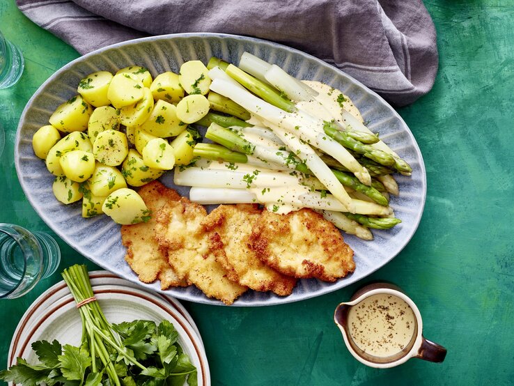 Auf einer Platte ist eine Portion Spargelplatte mit Hähnchenschnitzel angerichtet. Sie ist mit Petersilie verfeinert.