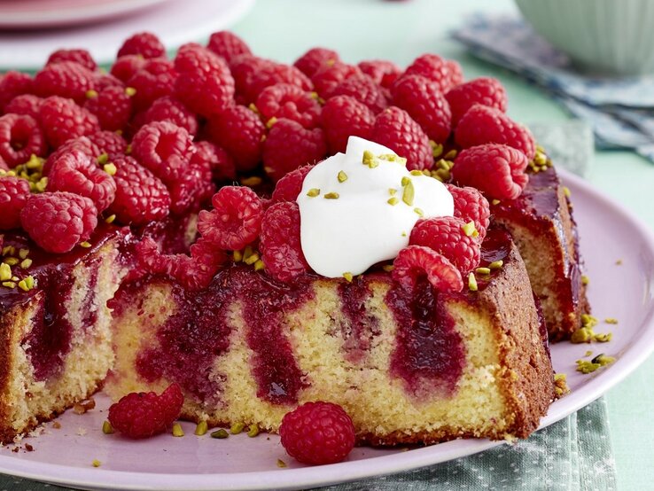 Auf einem pinken Teller liegt ein Himbeer-Zitrus-Kuchen. Er ist mit einem Klecks Schlagsahne bedeckt.