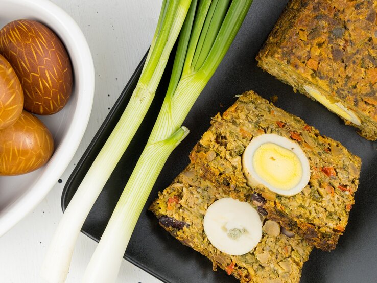 Vegetarischer Braten mit Ei auf einem schwarzen Brett und hellem Untergrund.