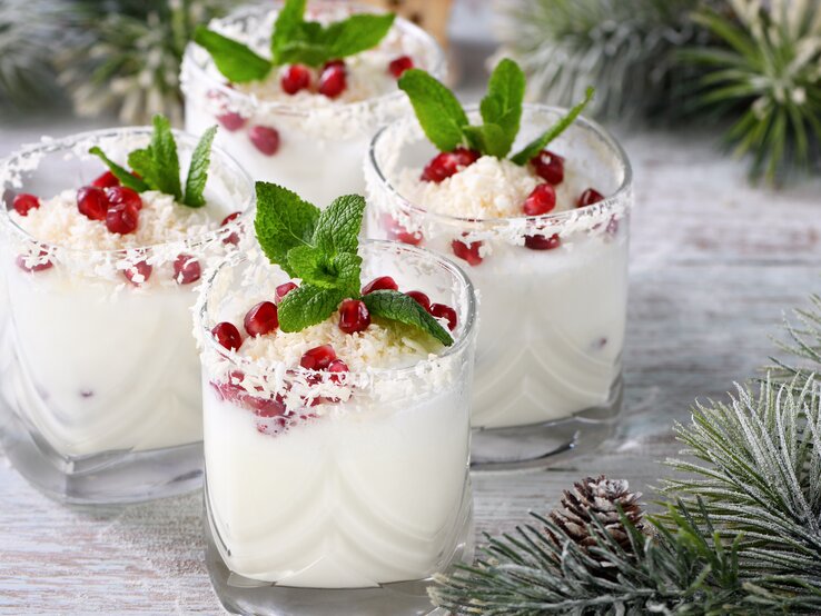 Vier Gläser White Christmas Mojito mit Minze und Granatapfelkernen sowie weißer Schokolade dekoriert. Drumherum weihnachtliche Deko.
