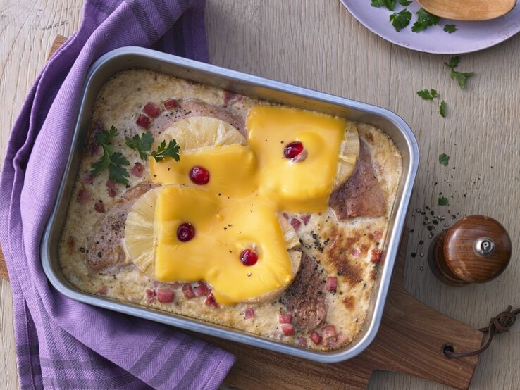 In einer Auflaufform ist ein Hawaii-Schnitzel mit Ananas angerichtet. Es ist mit Petersilie garniert.