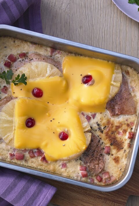 In einer Auflaufform ist ein Hawaii-Schnitzel mit Ananas angerichtet. Es ist mit Petersilie garniert.