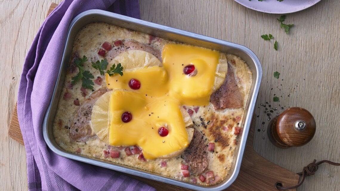 In einer Auflaufform ist ein Hawaii-Schnitzel mit Ananas angerichtet. Es ist mit Petersilie garniert.