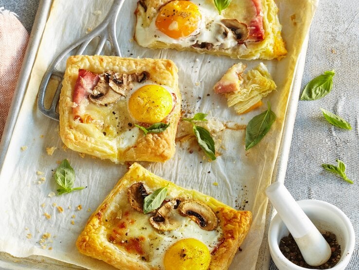 Blätterteigpizzen auf weißem Blech mit Gewürzmörser auf Mikrofaserdecke.