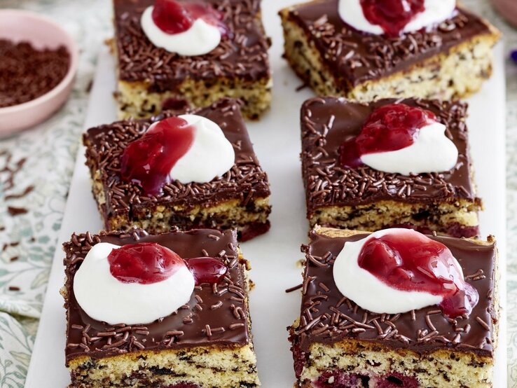 Auf einer Platte liegen mehrere Stücke des Kirsch-Ameisenkuchen. Er ist mit Sahne und roter Grütze verziert.