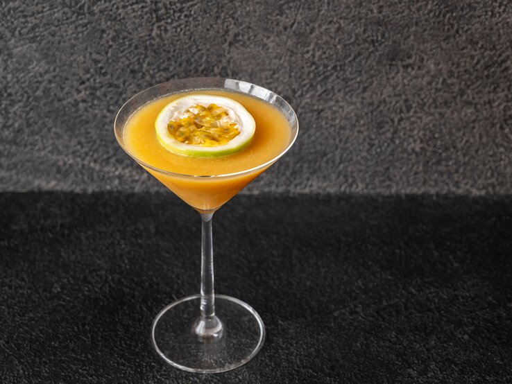 Martiniglas gefüllt mit orangefarbenem Cocktail vor dunkler Kulisse.