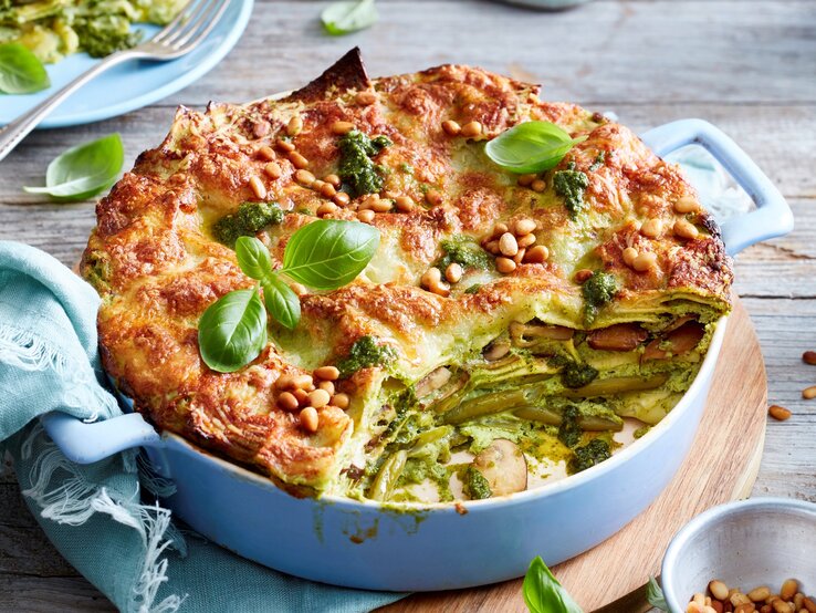 Ein hellblauer Topf mit Pesto-Lasagne auf einem Holzbrett.