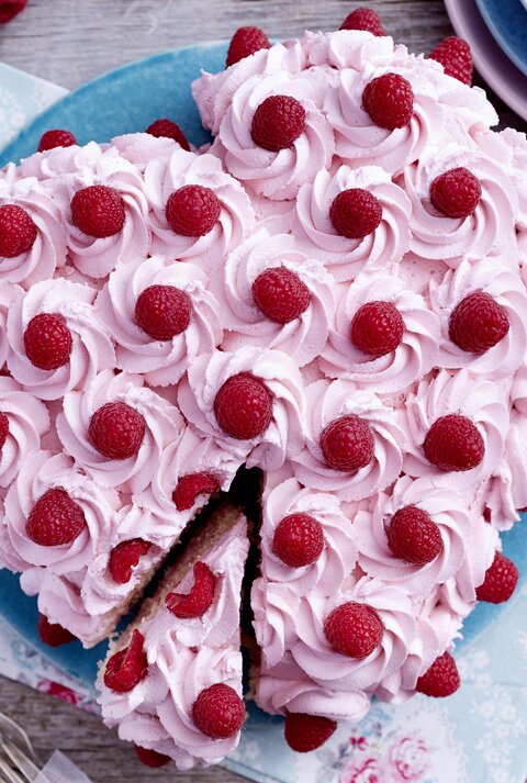 Herz-Himbeertorte auf einem blauen Teller auf hölzernem Hintergrund. 