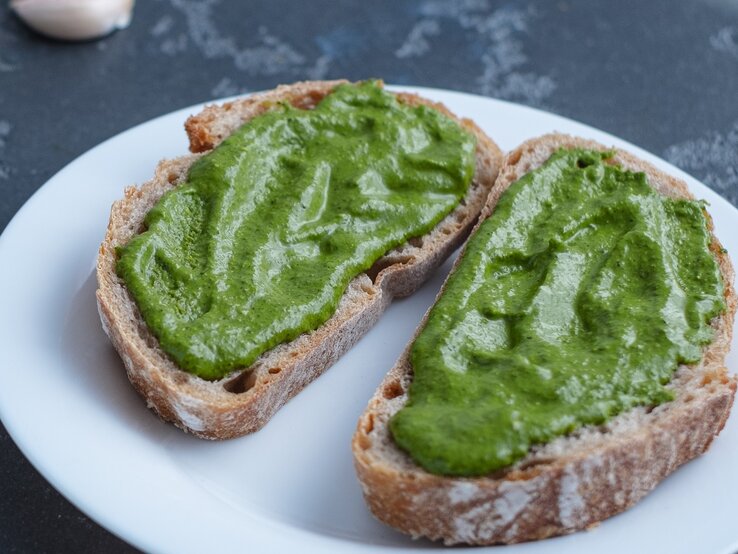 Ein weißer Teller mit zwei Brotscheiben und der grünen Avocado-Bärlauch-Creme.