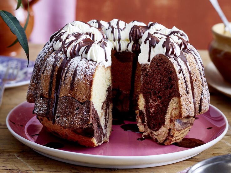 Auf einem Teller liegt ein angeschnittener Baileys-Marmorkuchen. Er ist mit Sahnetüpfeln verziert und mit Schokolade überzogen. 