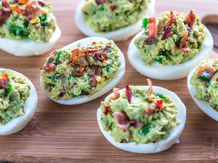 Sieben gefüllte Eier mit Avocado und Bacon auf Holzbrett. Aufnahme aus der Vogelperspektive.