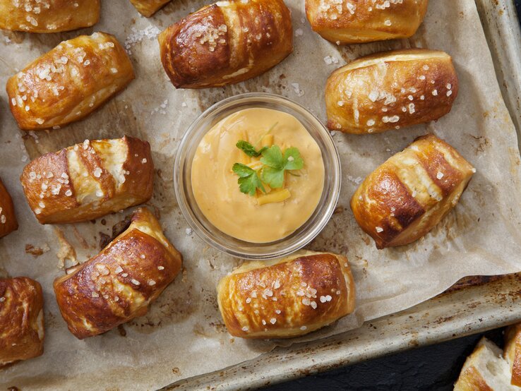 Selbstgemachte Bretzel-Happen auf einem Backblech mit Backpapier neben einer Schüssel mit Käsedip. 