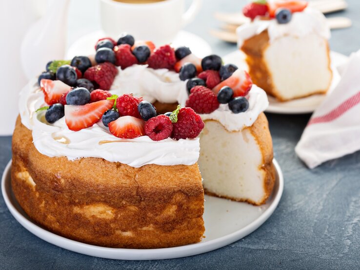 Heller Biskuitkuchen mit Creme und Beeren, angeschnitten, auf dunklem Untergrund. 