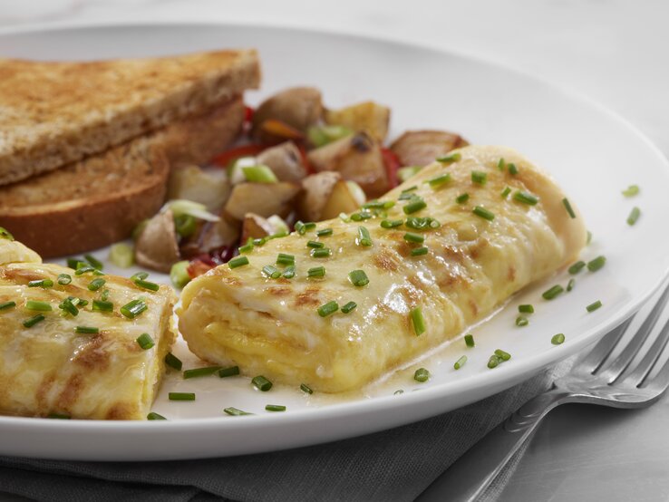 Käseomelett mit Schnittlauchröllchen auf Teller neben Toast-Brot.