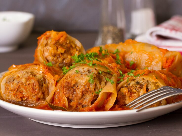 Ein weißer Teller mit den Kohlrouladen auf einem dunklen Holztisch.