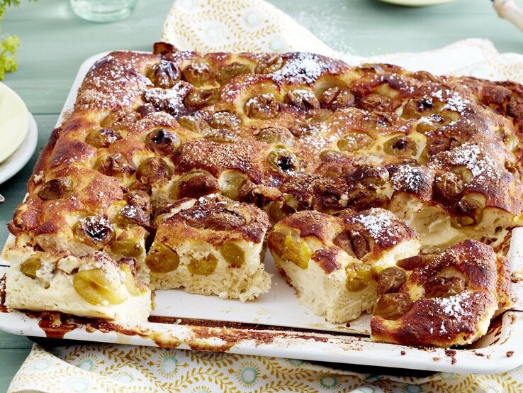 Auf einem Backblech liegt ein Mirabellen-Blechkuchen. Er ist mit Puderzucker bestreut. 
